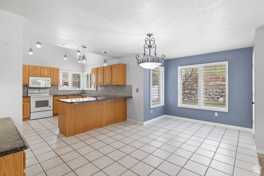 Kitchen with white appliances, kitchen peninsula, light tile flooring, and decorative light fixtures