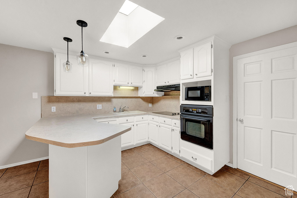 Kitchen featuring decorative light fixtures, white cabinets, black appliances, kitchen peninsula, and a skylight
