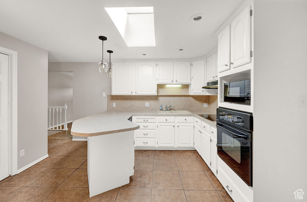 Kitchen featuring hanging light fixtures, white cabinetry, black appliances, light tile floors, and tasteful backsplash