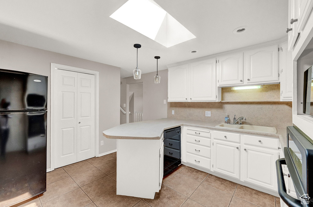 Kitchen featuring a skylight, white cabinetry, decorative light fixtures, black refrigerator, and kitchen peninsula