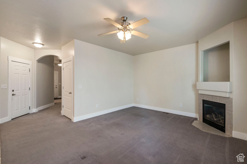 Unfurnished living room featuring dark colored carpet, ceiling fan, and a tiled fireplace