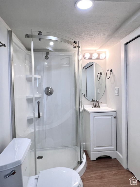 Bathroom featuring a textured ceiling, an enclosed shower, vanity with extensive cabinet space, and hardwood / wood-style flooring