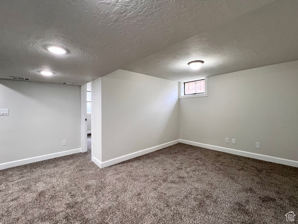 Basement with a textured ceiling and dark colored carpet
