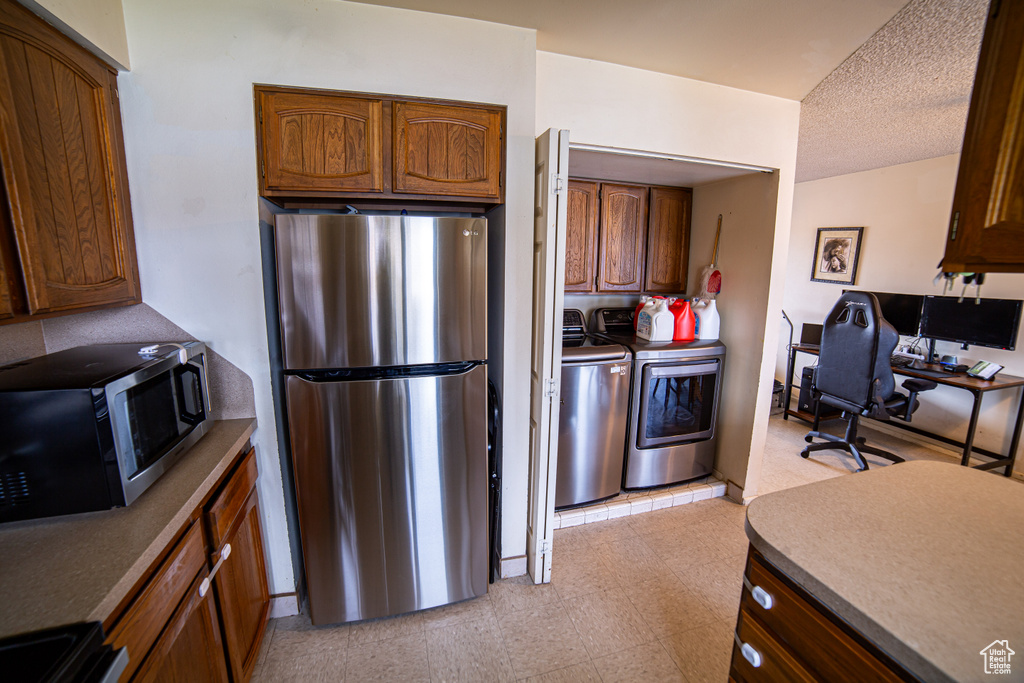 Kitchen with independent washer and dryer, appliances with stainless steel finishes, and light tile floors
