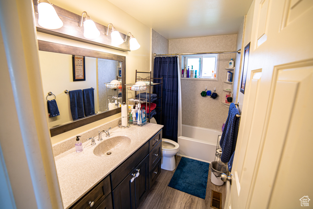 Full bathroom featuring hardwood / wood-style flooring, shower / bath combo with shower curtain, toilet, and vanity