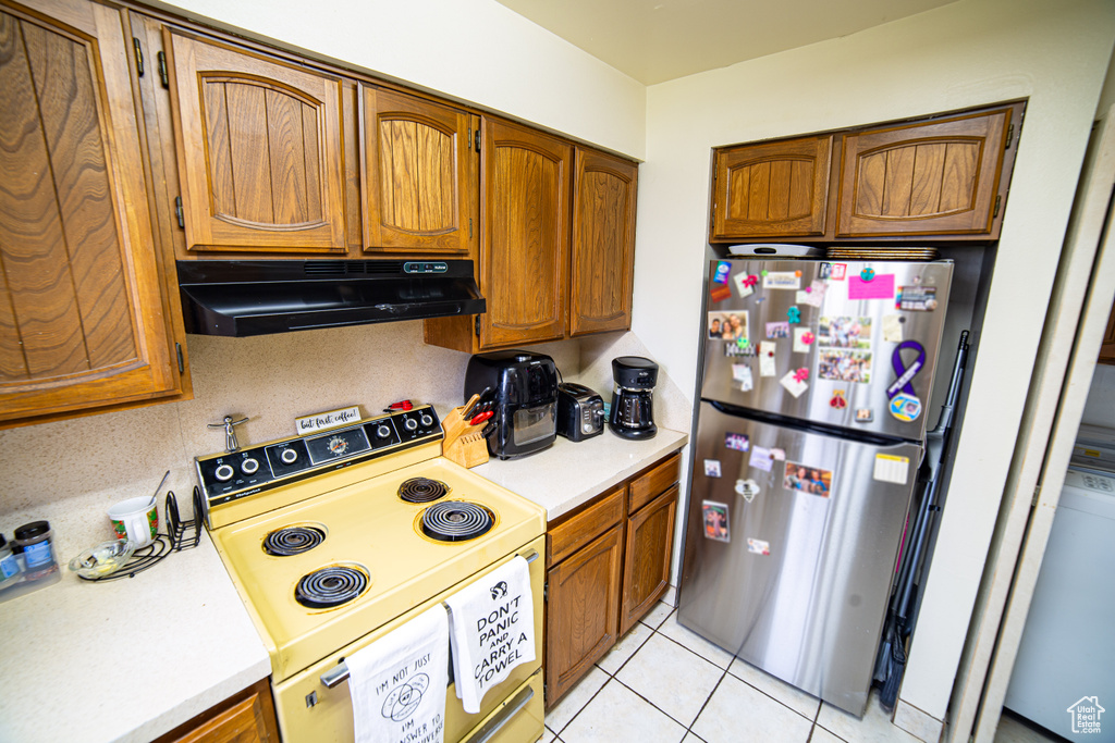 Kitchen with exhaust hood, stainless steel refrigerator, light tile floors, and electric range