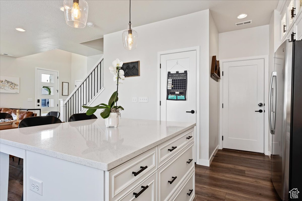 Kitchen featuring pendant lighting, light stone countertops, dark wood-type flooring, white cabinetry, and stainless steel fridge