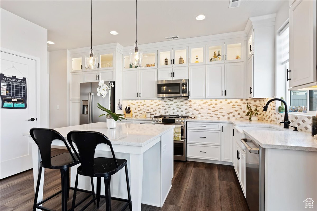 Kitchen with a center island, white cabinets, dark hardwood / wood-style floors, backsplash, and stainless steel appliances