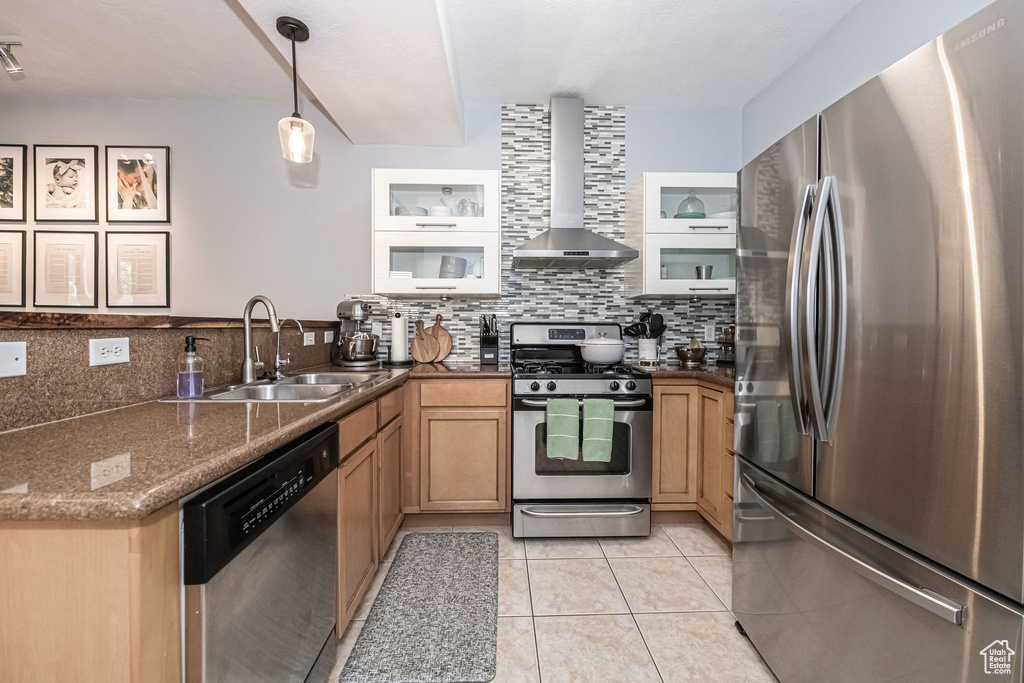 Kitchen with backsplash, stainless steel appliances, wall chimney range hood, sink, and light tile floors