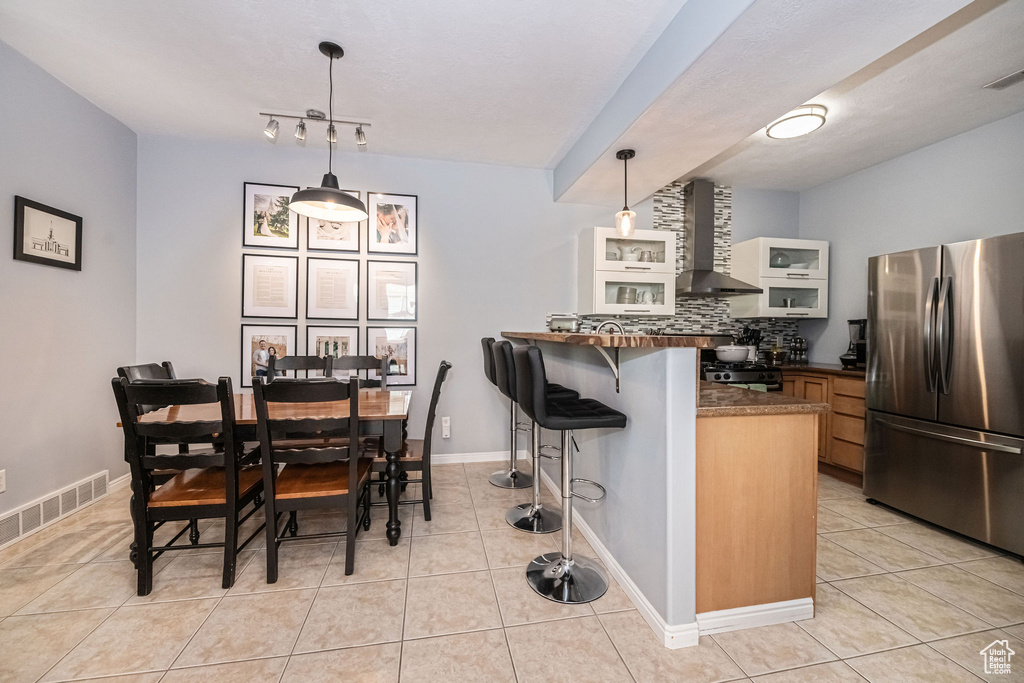 Kitchen featuring range, light tile flooring, wall chimney range hood, tasteful backsplash, and stainless steel fridge
