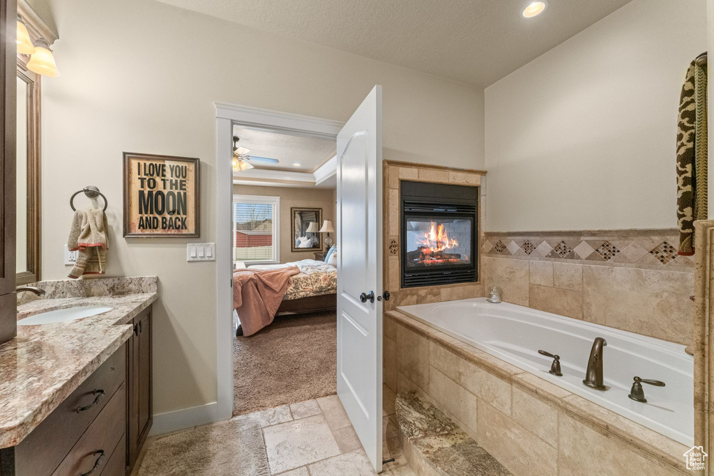 Bathroom featuring ceiling fan, a multi sided fireplace, tiled tub, tile floors, and vanity