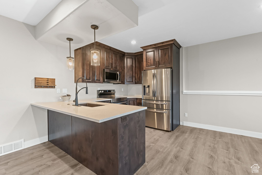 Kitchen featuring hanging light fixtures, stainless steel appliances, light hardwood / wood-style floors, and kitchen peninsula