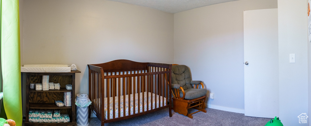 Carpeted bedroom featuring a nursery area and a textured ceiling