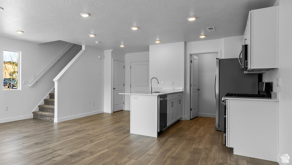 Kitchen featuring white cabinetry, dark hardwood / wood-style floors, appliances with stainless steel finishes, sink, and a center island with sink