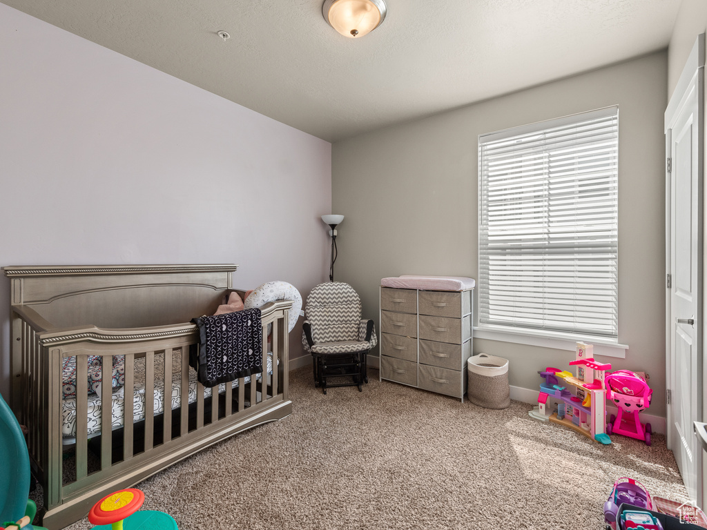 Bedroom featuring light colored carpet, a crib, and multiple windows