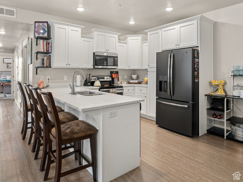 Kitchen with appliances with stainless steel finishes, a breakfast bar area, light hardwood / wood-style floors, white cabinets, and sink