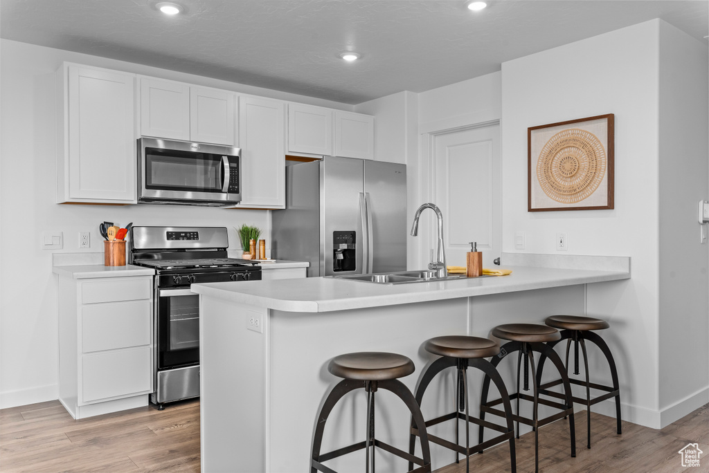 Kitchen with white cabinets, light hardwood / wood-style floors, appliances with stainless steel finishes, and a kitchen breakfast bar