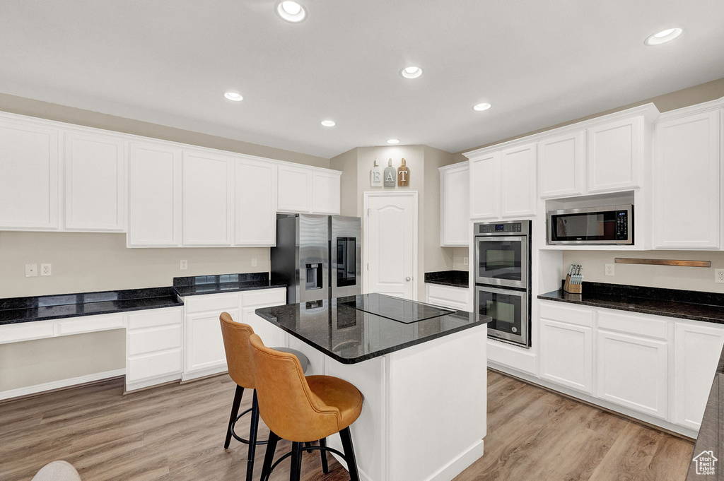 Kitchen with appliances with stainless steel finishes, light hardwood / wood-style flooring, a kitchen island, and white cabinets