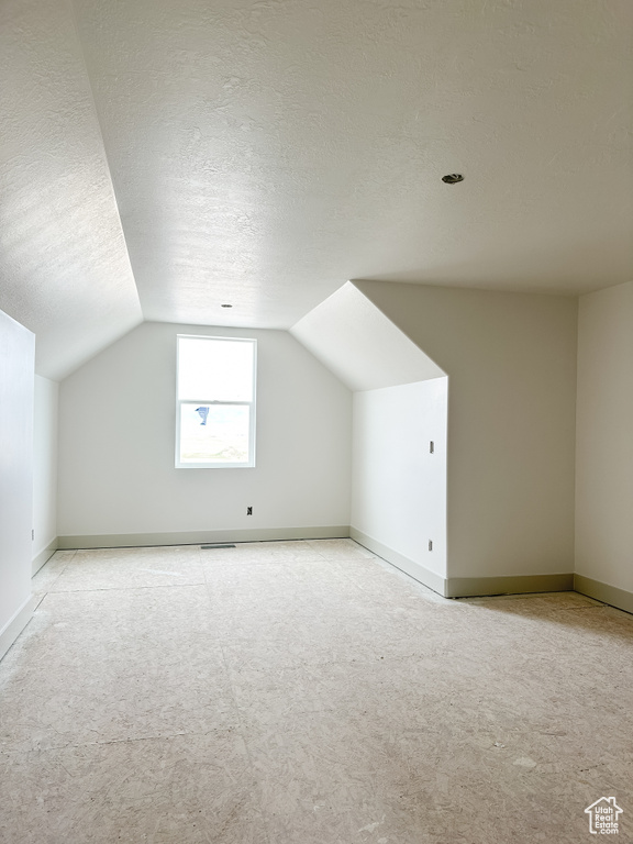 Additional living space with light colored carpet, a textured ceiling, and lofted ceiling