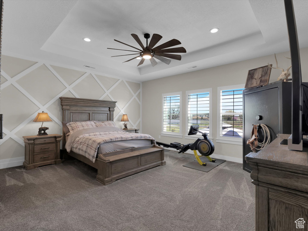 Bedroom featuring dark colored carpet, ceiling fan, and a tray ceiling