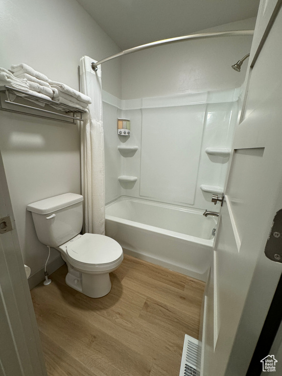 Bathroom featuring hardwood / wood-style floors, toilet, and shower / tub combo with curtain