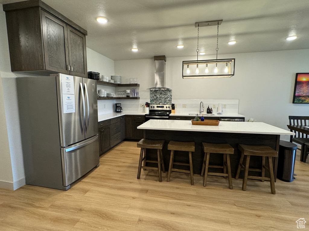 Kitchen featuring light hardwood / wood-style floors, wall chimney exhaust hood, and stainless steel appliances