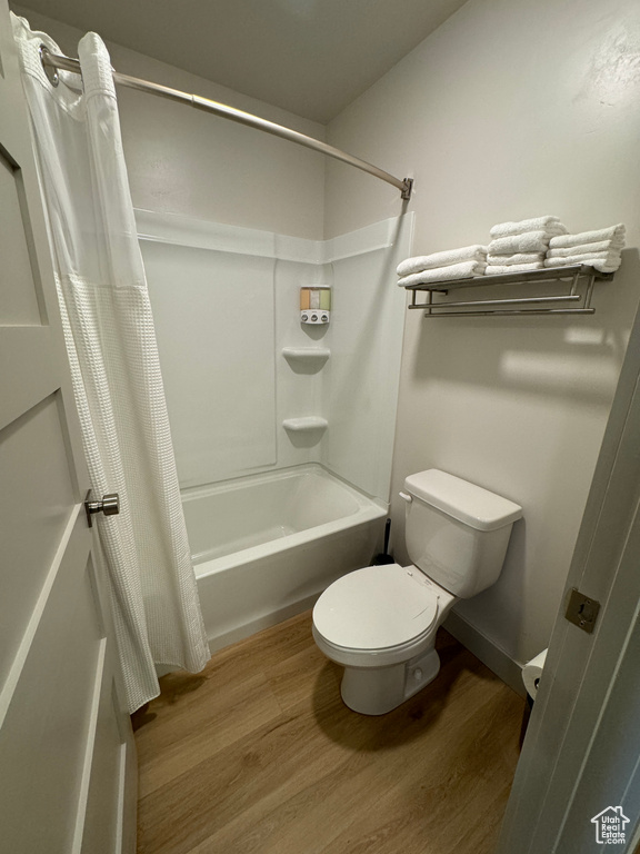 Bathroom with wood-type flooring, shower / bath combo with shower curtain, and toilet