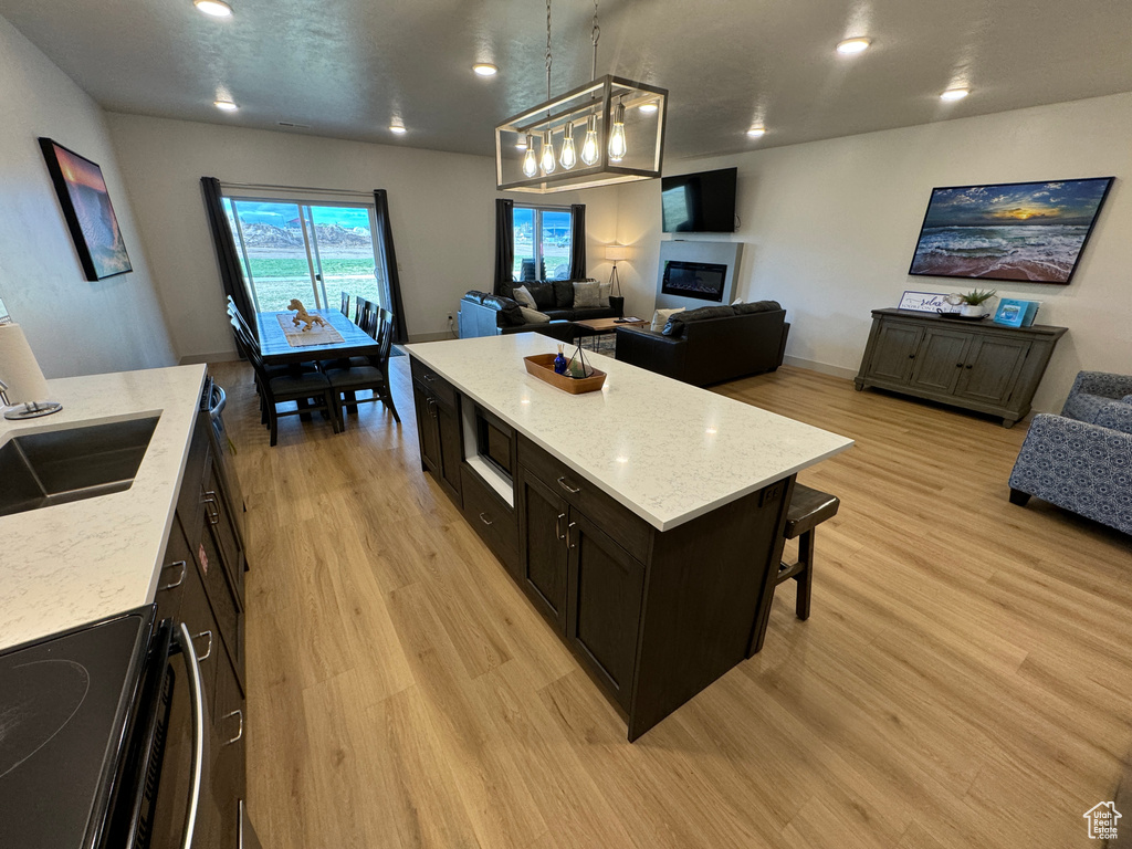 Kitchen featuring light stone countertops, a kitchen bar, hanging light fixtures, light hardwood / wood-style flooring, and range