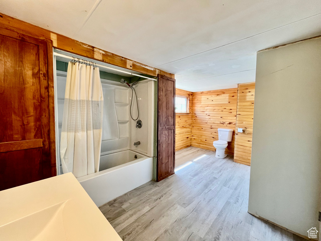 Bathroom with wooden walls, shower / bathtub combination with curtain, and hardwood / wood-style flooring