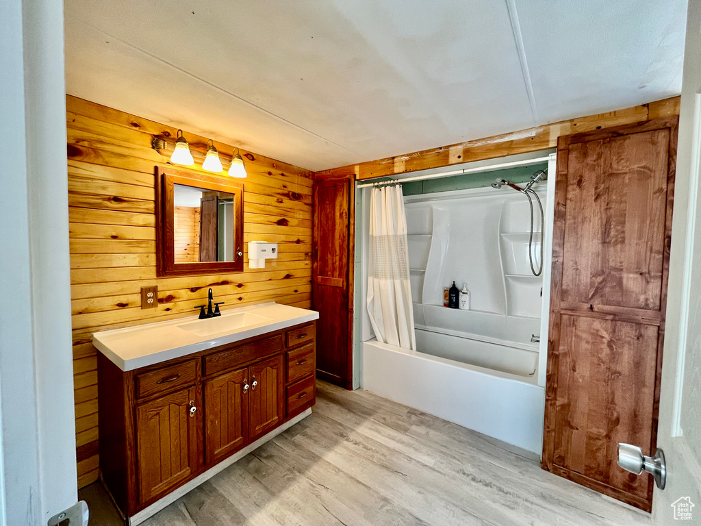 Bathroom featuring hardwood / wood-style floors, shower / tub combo, vanity, and wooden walls