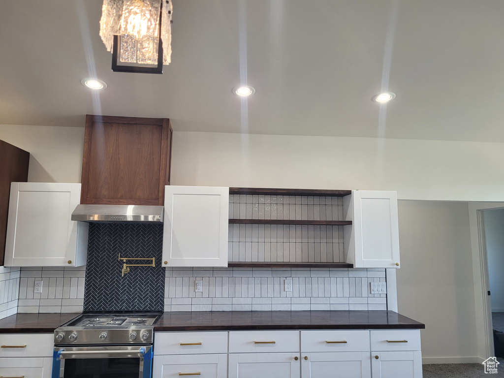 Kitchen featuring white cabinets, tasteful backsplash, wall chimney range hood, and high end stove