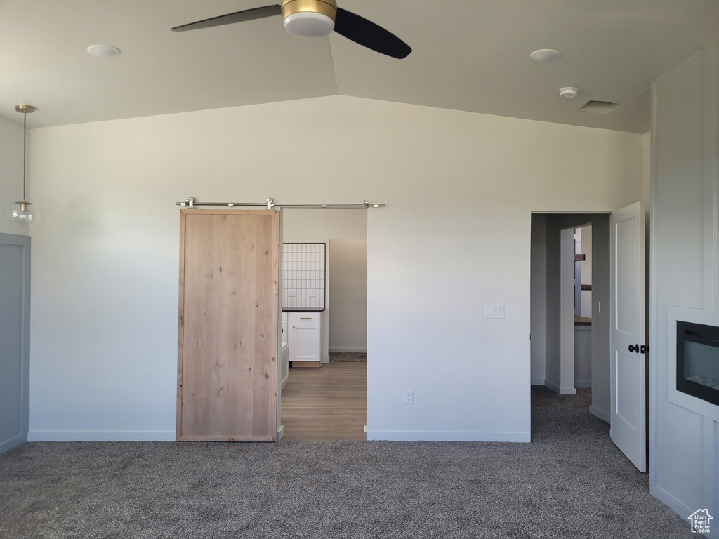 Spare room with dark colored carpet, a barn door, ceiling fan, and vaulted ceiling