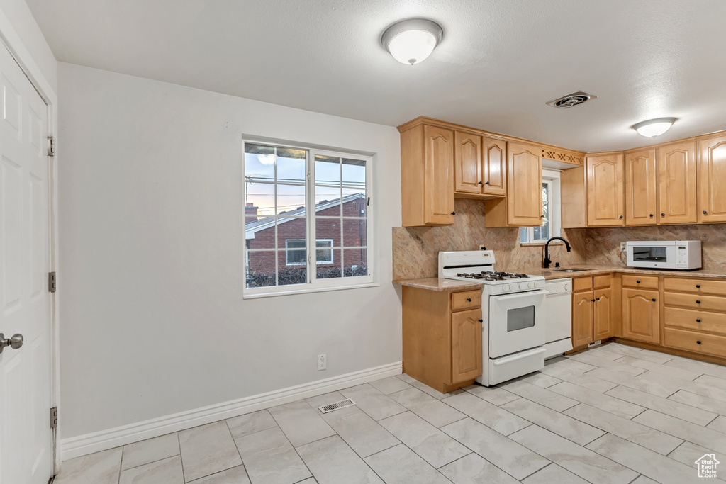 Kitchen with light brown cabinets, sink, white appliances, light tile flooring, and tasteful backsplash