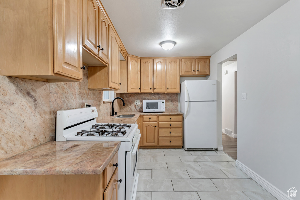 Kitchen featuring white appliances, light brown cabinets, backsplash, light tile floors, and sink