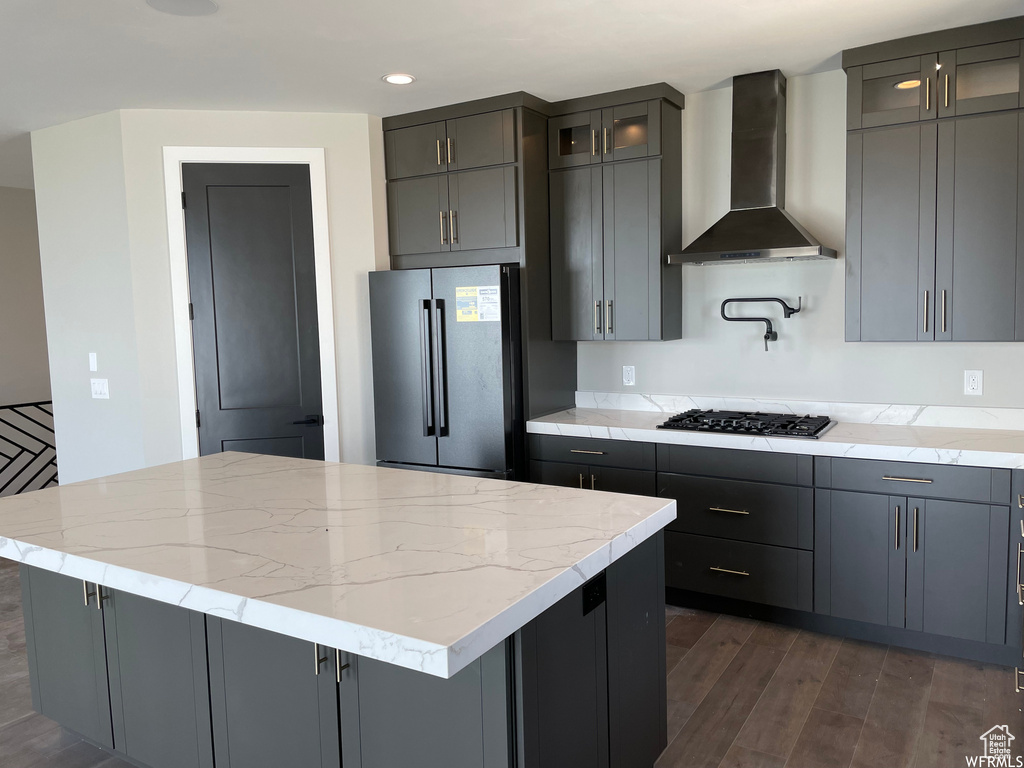 Kitchen with light stone counters, a kitchen island, wall chimney range hood, dark hardwood / wood-style floors, and high quality fridge