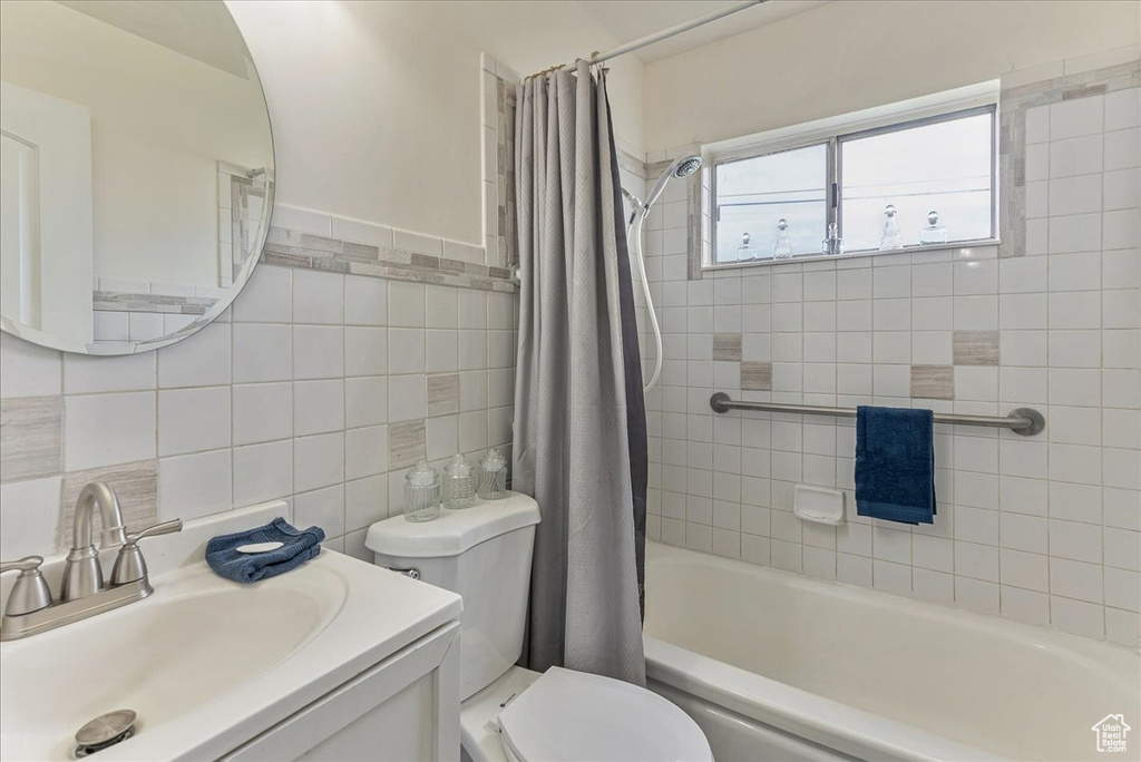 Full bathroom with tile walls, backsplash, shower / tub combo with curtain, toilet, and vanity