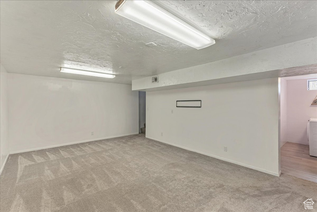 Basement featuring washer / clothes dryer, light carpet, and a textured ceiling