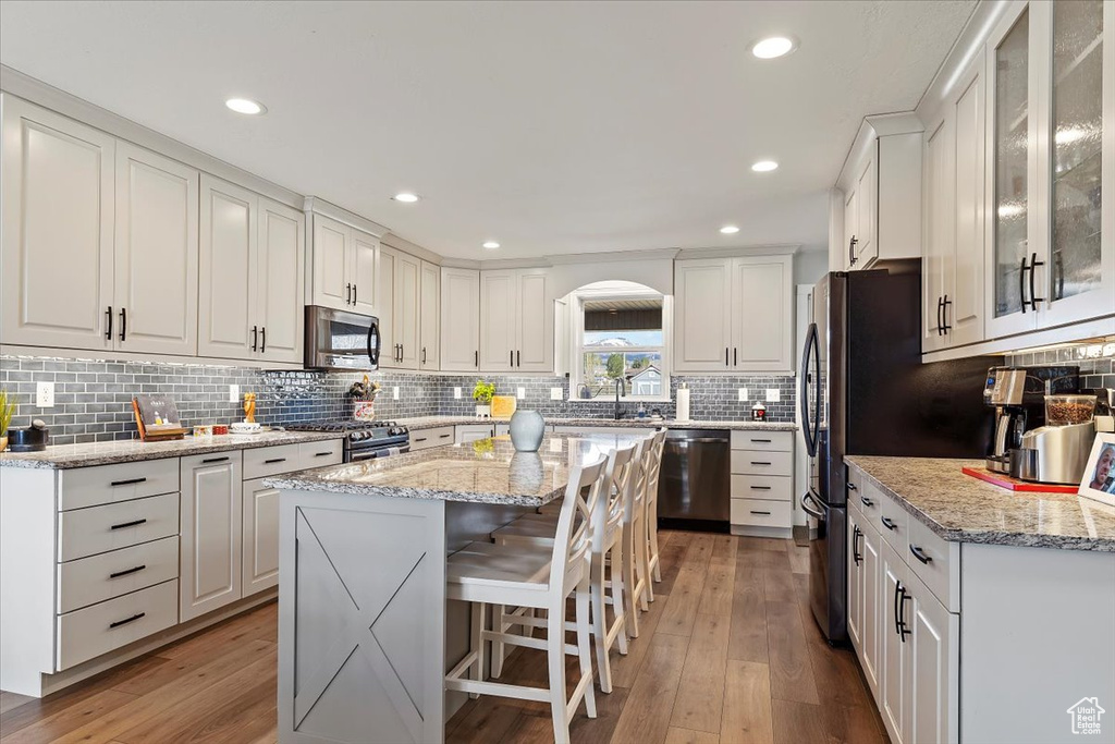 Kitchen with appliances with stainless steel finishes, wood-type flooring, a kitchen island, and white cabinets