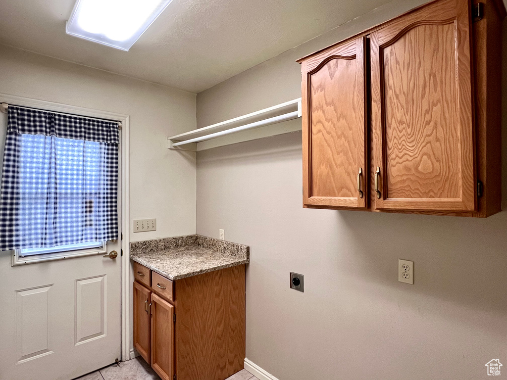 Clothes washing area with cabinets, hookup for an electric dryer, and light tile flooring