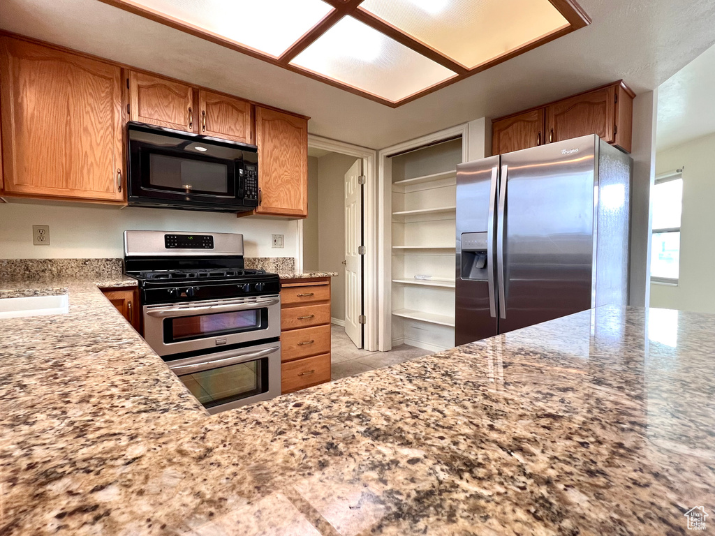 Kitchen with stainless steel appliances, light tile floors, and light stone countertops