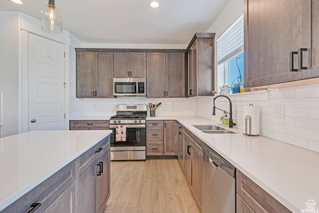 Kitchen with sink, light hardwood / wood-style floors, backsplash, decorative light fixtures, and stainless steel appliances
