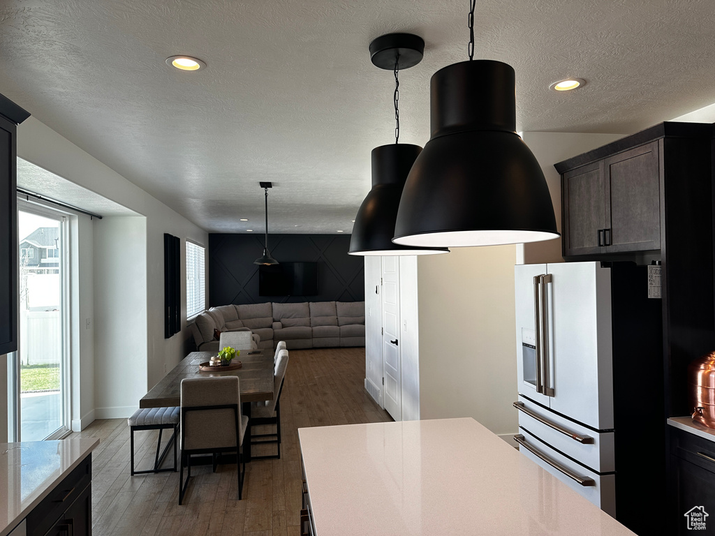 Kitchen with a textured ceiling, dark brown cabinets, dark hardwood / wood-style flooring, high end white refrigerator, and pendant lighting