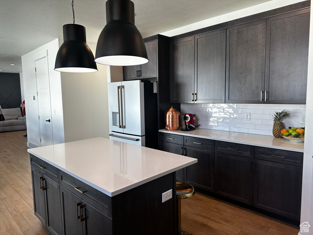 Kitchen with a kitchen bar, light hardwood / wood-style floors, a kitchen island, tasteful backsplash, and high quality fridge