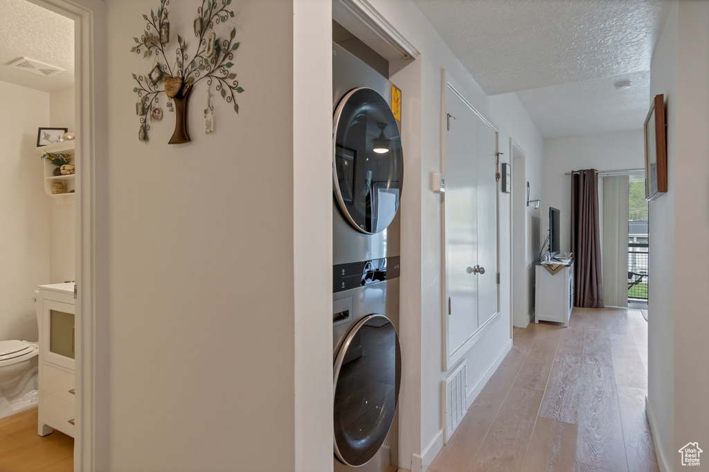Clothes washing area featuring light hardwood / wood-style floors, stacked washer / dryer, and a textured ceiling
