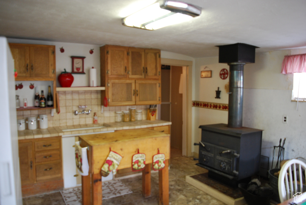 Kitchen featuring tile flooring, sink, tasteful backsplash, tile countertops, and a wood stove