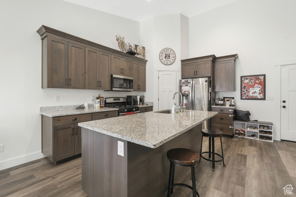 Kitchen with a kitchen breakfast bar, a kitchen island with sink, dark hardwood / wood-style floors, appliances with stainless steel finishes, and light stone counters