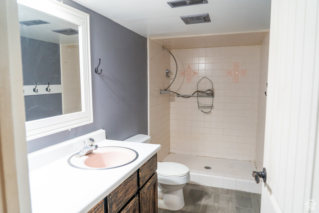 Bathroom featuring toilet, vanity, hardwood / wood-style floors, and a tile shower