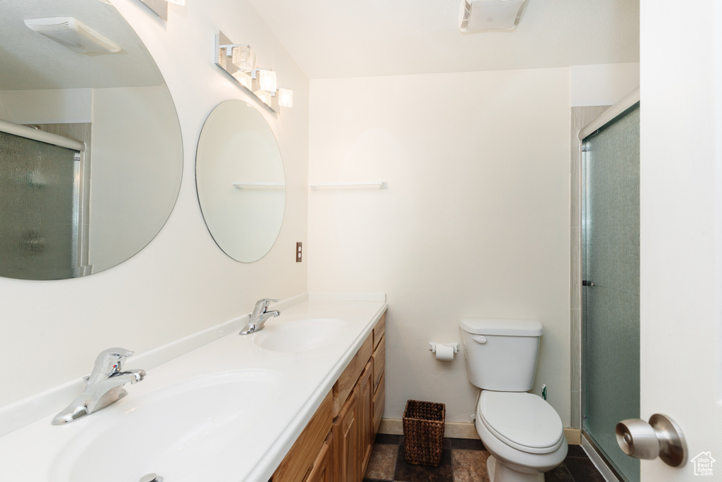 Bathroom with oversized vanity, double sink, tile floors, toilet, and a shower with door