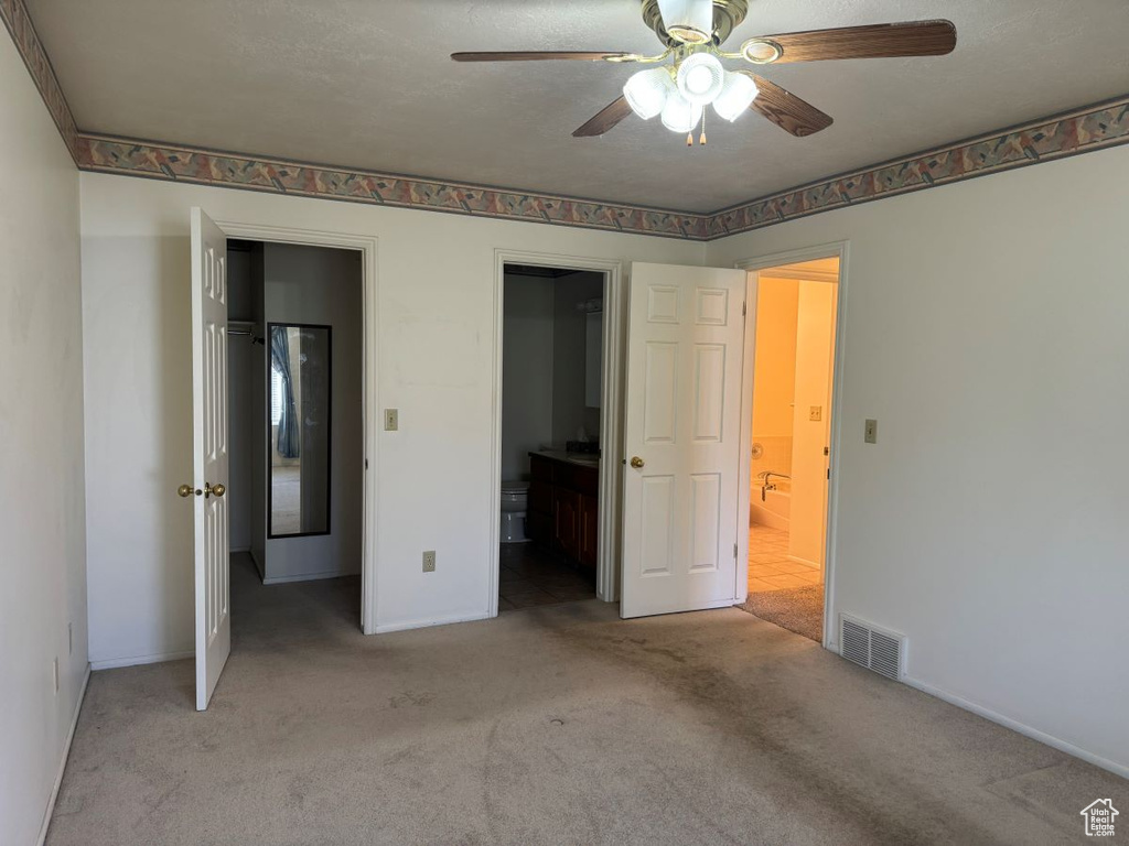Unfurnished bedroom with light colored carpet, ceiling fan, and ensuite bathroom