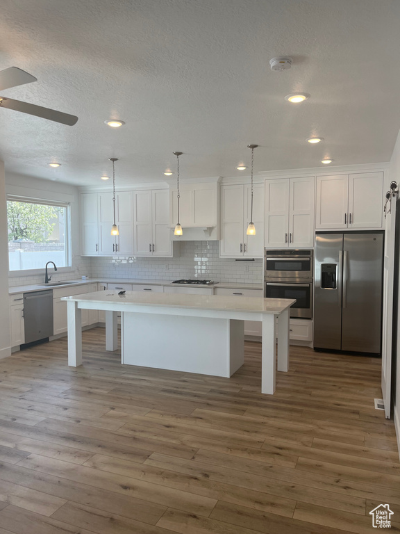 Kitchen featuring a center island, wood-type flooring, decorative light fixtures, stainless steel appliances, and ceiling fan